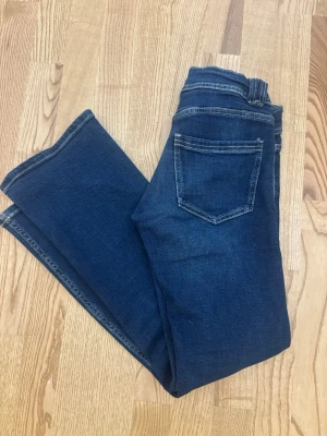 Mörkblå bootcut jeans med fickor - Snygga mörkblå bootcut jeans med klassiska bakfickor och kontrastsömmar. Jeansen har en lätt utsvängd passform nertill och är tillverkade i denim med stretch för extra komfort. Köpta från Gina barn, storlek 152
