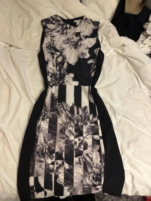 Svartvit blommig klänning H&M - Snygg svartvit kortklänning från H&M med blommigt och randigt mönster. Klänningen är ärmlös och har en figurnära passform som framhäver siluetten. Perfekt för dig som gillar stilrena kontraster och unika detaljer.