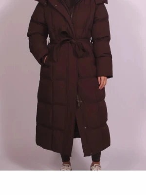 Lång brun pufferjacka ny - Säljer en lång och varm pufferjacka i mörkbrunt med stor huva och bälte i midjan. dragkedja och knappar framtill. Perfekt för kalla dagar och har en riktigt chill oversized vibe. Oanvänd då jag råkade beställa 2. Storlek xs men passar nog alla från xs till medium. Köpt för 1300kr