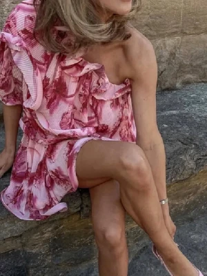 Rosa one shoulder klänning med volang - Superfin kortklänning i rosa och rött med blommigt mönster och volangdetaljer. Klänningen har oneshoulder-design och är tillverkad i ett lätt, plisserat material som ger en luftig känsla. Perfekt för dig som vill sticka ut med en färgstark look.