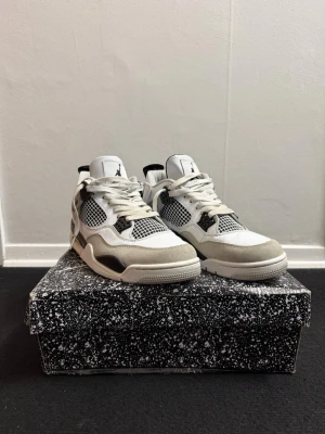 Air Jordan 4 military black - Snygga Air Jordan 4 military black sneakers i vitt, grått och svart. Skorna har meshpaneler, mockadetaljer och klassisk Jumpman-logga på plösen och hälen. Tjock sula och ikoniska plastdetaljer vid snörningen ger en sportig vibe. Använda ett par gånger men är fortfarande i bra skick. Kan även passa storlek 41.