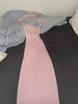 Ljusrosa halterneck långklänning - Supersöt ljusrosa långklänning med knyt i nacken och smala axelband. Klänningen har en enkel, rak passform 