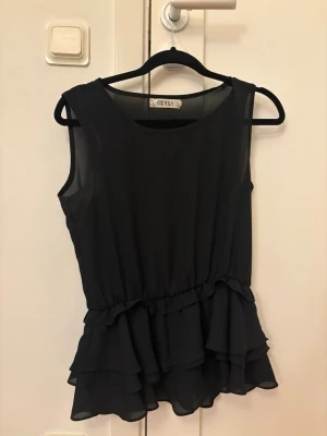 Svart volangblus  - Snygg svart blus från OXYEA med volangdetaljer nedtill och ärmlös design.  str står ej men passat mig som har str S