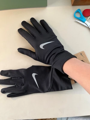 Svarta Nike pacer lightweight gloves - Svarta, tunna och smidiga löparhandskar från Nike med reflekterande logga på ovansidan. Perfekta för utomhusträning när det är lite kyligt. Snygg och sportig design som passar dig som gillar att röra på sig nu i kylan 