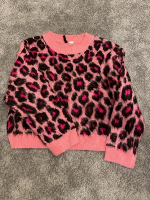 Rosa leopardmönstrad stickad tröja - Cool stickad tröja från Divided i rosa med svart och mörkrosa leopardmönster. Tröjan har rund halsringning, ribbade muddar och en loose passform. Perfekt för dig som vill sticka ut med ett djurmönster och färg!