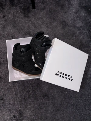 Isabel Marant Skor - Snygga svarta high top sneakers från Isabel Marant med cool design och kardborreband. Skorna har en mix av mocka och läder, samt en brun sula som ger en schysst kontrast. Perfekta för dig som vill ha en edgy och trendig look.