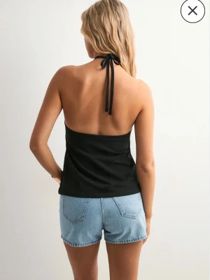 Två halterneck toppar - 1 svart och 1 vit halterneck topp med knyt i nacken och öppen rygg. Toppen är ärmlös och har en stilren, tight passform som passar perfekt till jeansshorts eller kjol. Enkel och trendig design som är lätt att matcha.