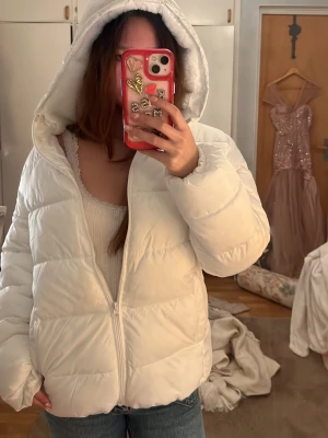 Vit pufferjacka med huva från mango - Säljer en fluffig vit pufferjacka från mango med dragkedja och stor huva. Jackan har quiltad design och två sidofickor med dragkedja. Perfekt för kalla vinterdagar och riktigt mysig att bära. Materialet är syntetiskt och jackan är fodrad för extra värme.