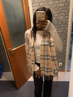 Beige rutig halsduk med fransar - Snygg beige halsduk med klassiskt rutmönster i svart, vitt och rött. Skulle inte säga att den är varm utan bra till stajling 