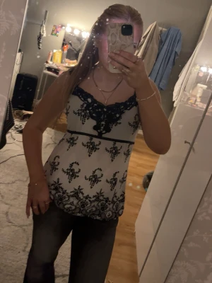 Vit och svart spetslinne med mönster - Snyggt vitt linne med svarta spetsdetaljer och dekorativt mönster. Djup V-ringning med spetskant och lite bredare axelband. 