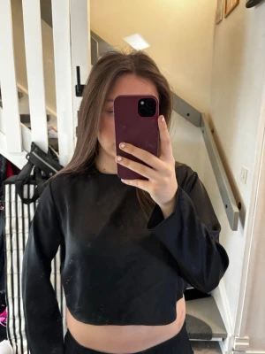 Svart croppad långärmad topp - Snygg svart croppad topp med långa ärmar och rund halsringning. Toppen har en stilren och minimalistisk design, perfekt att matcha med höga jeans eller kjol. Materialet känns slätt och har en lätt glansig finish.💖