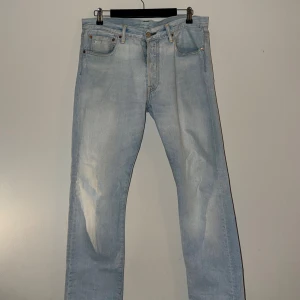 Ljusblå raka jeans från Levi's - Säljer ett par klassiska ljusblå jeans från Levi's med rak passform och fem fickor. Jeansen har gylf med knapp och dragkedja samt Levi's ikoniska läderpatch bak i midjan. Perfekta för en avslappnad stil.