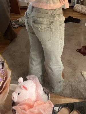 Ljusgrå raka jeans med fickdetalj - Säljer ett par ljusgrå jeans med rak passform och snygga fickdetaljer bak. Jeansen har klassisk femficksdesign och normal midja. Perfekta för en avslappnad och trendig look.