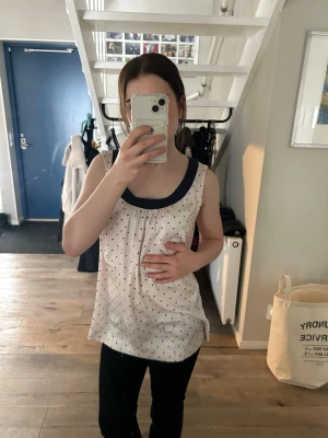 Prickig ärmlös topp med marinblå kant - Säljer en söt ärmlös topp från H&M i ljusrosa med små marinblåa prickar och en bred marinblå kant runt halsen. Toppen har en lös passform och är perfekt för varma dagar. Superfin att styla med jeans eller kjol!