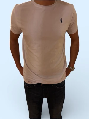 Vit t-shirt från Ralph Lauren - Klassisk vit t-shirt från Ralph Lauren med rund halsringning och korta ärmar. Diskret broderad logga i mörkblått på bröstet. Tillverkad i mjuk bomull för en bekväm passform. Perfekt basplagg till garderoben. Står L på tröjan men den har krympt med tvätten så sitter som s