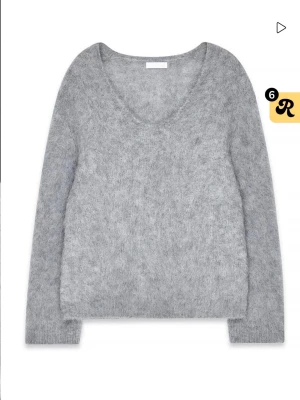 Ljusgrå fluffig stickad tröja - Mysig ljusgrå stickad tröja med fluffig känsla och rundad halsringning. Tröjan har långa ärmar och en avslappnad passform, perfekt för lager på lager. Materialet ser ut att vara en mjuk blandning, troligen med mohair eller liknande.