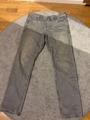 Grå raka jeans i vintage-look - Säljer ett par grå jeans med rak passform och klassisk femficksdesign. Jeansen har en snygg vintage-tvätt och är tillverkade i denim. Perfekta för dig som gillar en avslappnad och tidlös stil.