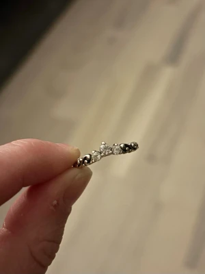 Silverring med stenar från Pandora - Snygg silverring från Pandora med glittrande stenar i olika storlekar framtill. Ringen har ett elegant, vågigt mönster och små detaljer längs bandet. Perfekt för dig som gillar stilrena accessoarer med lite extra bling.
