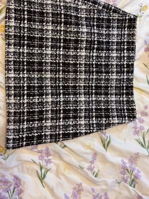 Svartvit rutig kortkjol - Säljer en svartvit kortkjol med rutigt mönster. Kjolen har en rak passform och är tillverkad i ett tjockare tyg som ger en snygg struktur. Perfekt att styla med en enkel topp eller stickad tröja.