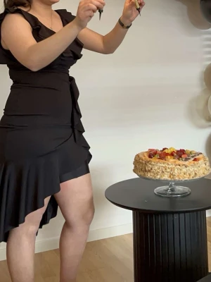 Svart omlottklänning med volang - Snygg svart omlottklänning med volangdetaljer och asymmetrisk nederkant. Klänningen har kort ärm och knyt i midjan för en smickrande passform. Perfekt för dig som vill ha en stilren men ändå lekfull look.