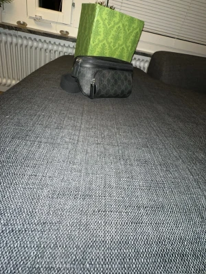 GG Svart midjeväska med dragkedja - Snygg svart midjeväska i konstläder med två fack och silverfärgade dragkedjor. Perfekt för att bära det viktigaste och enkel att justera runt midjan. Stilren och praktisk design som passar till det mesta.