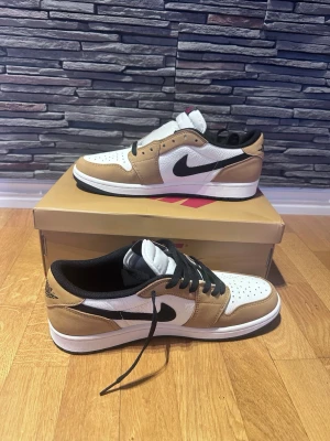 Nike Air Jordan 1 Low OG rookie of the year - Snygga Nike Air Jordan 1 Low OG i färgen Mocha med vit tåbox, bruna paneler och svart swoosh. Skorna har svart innersula och svarta skosnören. Klassisk låg siluett och tillverkade i läder och mocka för en clean och trendig look.