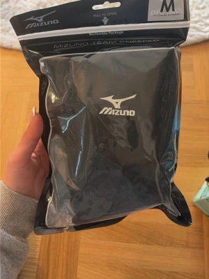 Svarta knäskydd från Mizuno - Säljer ett par svarta Mizuno Team knäskydd i storlek M. Perfekta för sport och träning, speciellt volleyboll. Tillverkade i slitstarkt material med Mizuno-logga framtill. Sitter bekvämt och ger bra stöd vid knäna. Oöppnade helt nya. Passar storlek S. 