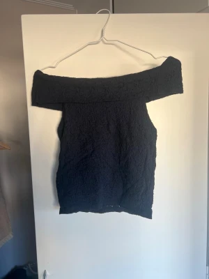 Svart offshoulder topp - Säljer en svart offshoulder topp med croppad passform och struktur i tyget. Perfekt för dig som vill ha en stilren och trendig look. Toppen är ärmlös och har en bred krage som sitter snyggt över axlarna. Storlek 158-164