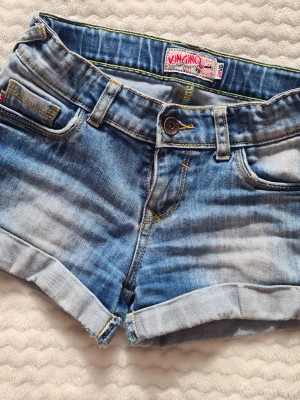 Lågmidjade jeanshorts från Vingino - Snygga blå jeansshorts från Vingino med klassisk femficksdesign och uppvikta benslut. Dom har låg midja och med en vintage stil. Perfekta för varma dagar och enkel att matcha med olika toppar.