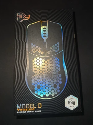 Glorious Model O Wireless Gamingmus - Trådlös gamingmus från Glorious, Model O Wireless, med matt vit finish och hexagonmönstrad design. Musen väger endast 69g, har RGB-belysning, 6 programmerbara knappar och BAMF-sensor med upp till 19 000 DPI. Utrustad med PTFE-skates och upp till 71 timmars batteritid.