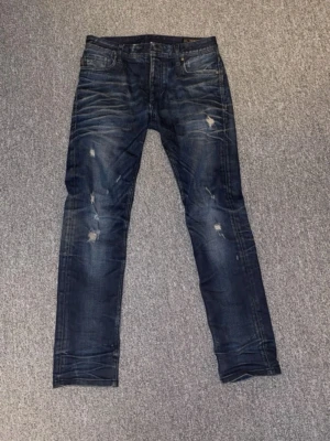Mörkblå slitna jeans  - Snygga mörkblå jeans från Jack & Jones med slim fit passform + klassiska slitningar. Storlek W29. OBS: Knappen som knäpper ihop jenasen saknas.
