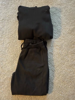 Gymshark  - Säljer ett snyggt mjukisset från gymshark, alltså både hoodie och byxor. Ett väldigt bekvämt set med loggan diskret på benet samt bröstet. Färgen är inte helt svart utan en snygg grå/svart.