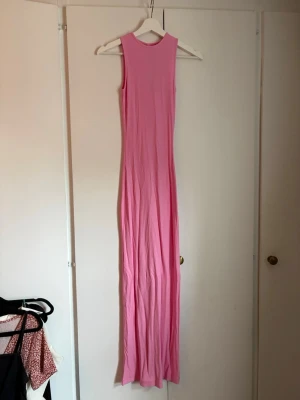 Rosa långklänning  - Säljer en lång, ärmlös klänning från skims i en snygg rosa färg. Klänningen är ribbad och har en rund halsringning. Perfekt för dig som gillar en enkel men trendig look.