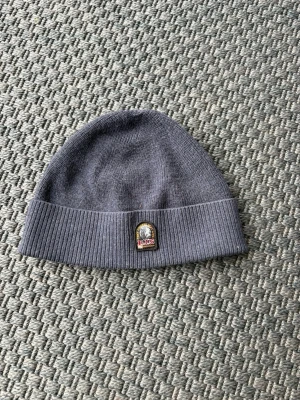 Blå Parajumpers Mössa - oanvänd - Säljer en stilren blå mössa från Parajumpers med uppvikt kant och ribbstickad nederdel. Mössan har en snygg patch med Parajumpers-loggan framtill. Perfekt för kalla dagar och enkel att matcha med olika outfits.