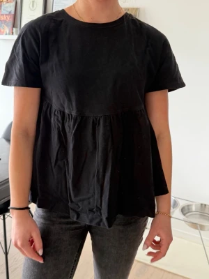 Svart volangtop från Zara - Svart topp från Zara med rund halsringning och korta ärmar. Toppen har en lös passform och volangdetalj. Tillverkad i mjuk bomull som känns skön mot huden✨ Det är en basic topp men den passar till allt!😍