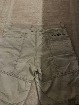 Beige shorts från Sail Racing - Snygga beige shorts från Sail Racing med klassisk design och flera fickor. Tillverkade i slitstarkt bomullsmaterial och har bälteshällor i midjan. Perfekta för varma dagar och en avslappnad stil.