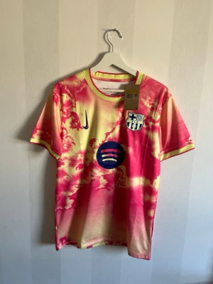 Barcelona matchtröja Balde #3 - Snygg FC Barcelona matchtröja från Nike med Balde och nummer 3 på ryggen. Tröjan har ett färgstarkt tie-dye mönster i rosa, gul och orange, klubbmärke och Nike-logga på bröstet samt Spotify-logga. Perfekt för dig som älskar fotboll och vill sticka ut på planen.