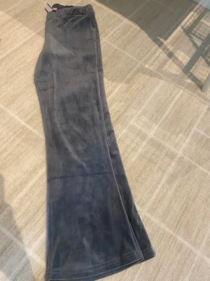 Grå velourbyxor från Vero Moda - Mysiga blå/grå mjukisbyxor i velour från Vero Moda med utsvängda ben och resår i midjan. Perfekta för chill dagar hemma eller när du vill ha en avslappnad stil. Materialet är mjukt och stretchigt för extra komfort. 