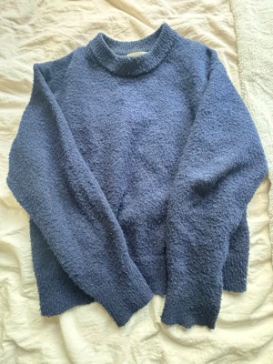 Blå stickad tröja från Gina tricot - Mysig blå stickad tröja med fluffig textur och rund hals. Tröjan har långa ärmar och ribbade muddar vid ärmslut och nederkant. Perfekt för dig som gillar en avslappnad och bekväm stil.