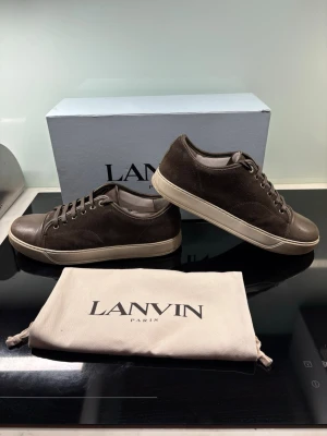 Bruna Lanvin sneakers i mocka och läder - Snygga bruna sneakers från Lanvin i en mix av mocka och läder. Skorna har klassisk låg profil, rund tå och beige sula. Perfekta för dig som gillar stilrena och exklusiva detaljer. Levereras med originalpåse och box.