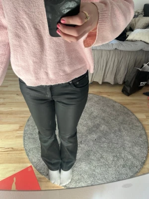 Svarta bootcut jeans - Säljer ett par svarta bootcut läderbyxor med klassisk femficksdesign. Läderbyxor har en snygg, något glansig finish och sitter tajt upptill med utsvängda ben. Perfekta för dig som vill ha en trendig och bekväm look.