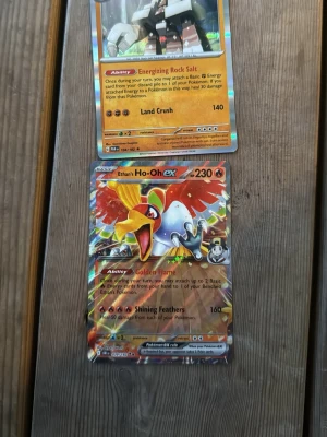 Pokémonkort Ho-Oh EX och Stonjourner - Två Pokémonkort: Ho-Oh EX med färgstark holografisk design och 230 HP samt Stonjourner med orange och silver detaljer och 140 HP. Båda korten har unika attacker och förmågor, perfekta för samlare eller Pokémonfans.
