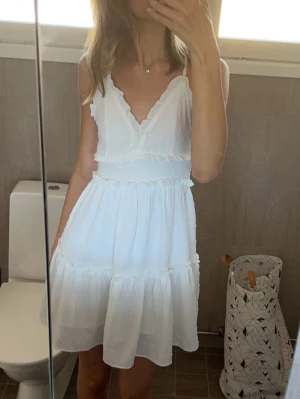 Vit studentklänning - Söt vit klänning med v-ringning och tunna axelband. Klänningen har volangdetaljer och är sydd i ett lätt, luftigt tyg som passar perfekt för varma dagar. Den har en feminin siluett och är kort i modellen. Skriv för fler bilder💞