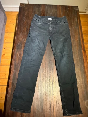 Svarta slim fit jeans - Snygga svarta slim fit jeans med klassisk femficksdesign och normalhög midja. Jeansen har raka ben och subtila slitningar för en avslappnad look. Passar perfekt till en streetwear-stil eller till vardagsoutfiten.