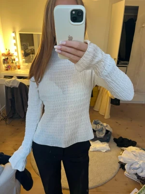Vit ribbad långärmad topp - Säljer en vit långärmad topp med ribbad struktur och hög hals. Tröjan har en figurnära passform och lätt utsvängda ärmslut. Perfekt för dig som gillar en clean och stilren look.