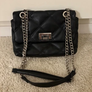 Svart quiltad väska med silverkedja – Stradivarius -  Snygg svart quiltad väska från Stradivarius med silverfärgad kedja. Perfekt till både vardag och fest – enkel att matcha med allt!    Väskan är i fint skick och har ett klassiskt, trendigt utseende. Lagom storlek för mobil, plånbok och andra essentials.    👜 Kan bäras både som axelväska och crossbody.    💌 Hör av dig vid frågor!    #