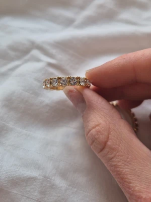 Guldfärgad ring med klara stenar - Snygg guldfärgad ring med flera klara, gnistrande stenar runt hela bandet. Båda är I Guld och säljer då jag märkte att båda är lite förstora när jag kom hem! Minns inte exakt vad de kostade men skulle gissa på 100-250 kr! MITT pris (för båda tillsammans) 80 kr! Köpt på glitter!