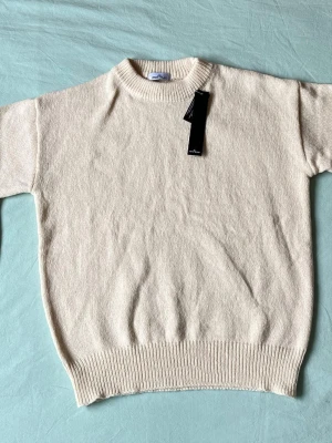 Vit stickad tröja från Stone Island - Säljer en stilren vit stickad tröja från Stone Island. Tröjan har rund halsringning, ribbade muddar och är gjord i ett mjukt material som känns lyxigt. Perfekt för dig som gillar minimalistisk och clean stil.