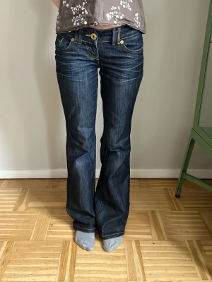 Mörkblå bootcut jeans från River Island - Säljer ett par jättesnygga mörkblå bootcut jeans i storlek 34 eller xs med snygga kontrastsömmar och dekorativa fickor bak. Jeansen har låg midja och en stor knapp vid gylfen. Byxbenen är lite slitna där nere men det är inget man tänker på.💕