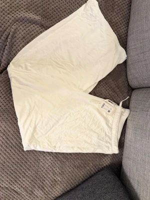 Vita loose shorts från H&M - Säljer ett par vita shorts från H&M med loose fit och elastisk midja med snörning. Perfekta för sommaren och riktigt sköna att bära. Materialet är mjukt och lätt, troligen bomull eller en bomullsblandning.